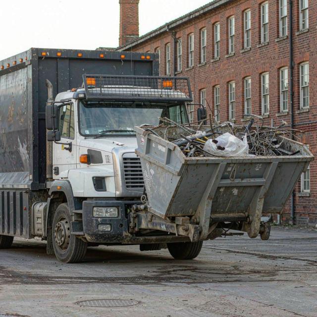 Roll-on roll-off skip lorry collecting a loaded metal skip from an industrial client premises